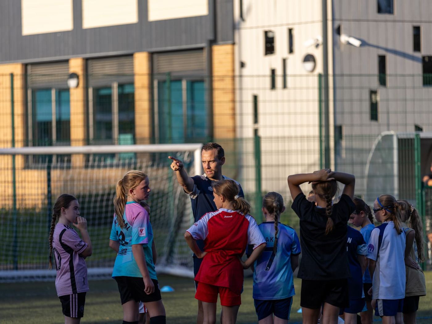 Coach briefing a group of young female players on a pitch